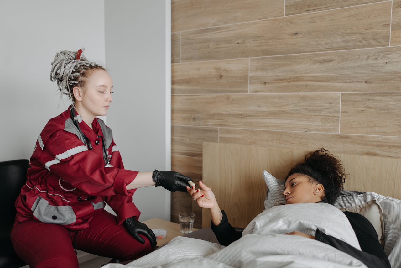 A paramedic provides care to a sick woman lying in bed, highlighting healthcare support at home.